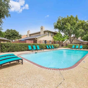 Pool with bright teal lounge furniture with large trees and beautiful blue sky in the background