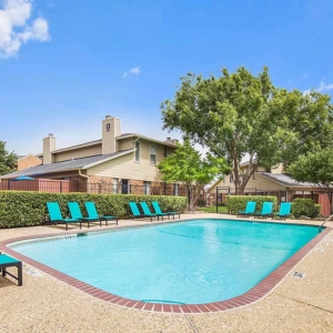 Pool with bright teal lounge furniture with large trees and beautiful blue sky in the background