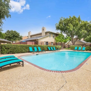 Pool with bright teal lounge furniture with large trees and beautiful blue sky in the background