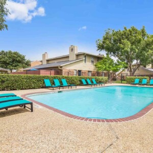Pool with bright teal lounge furniture with large trees and beautiful blue sky in the background