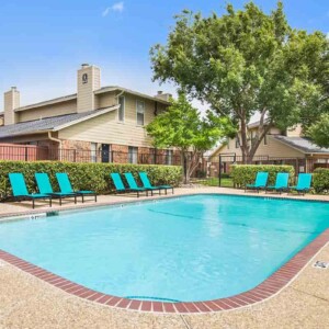Pool with bright teal lounge furniture with large trees and beautiful blue sky in the background